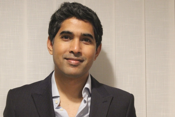 Humayon Pramanik, an Asian man, with short dark hair, smiles at the camera. He wears an open necked grey shirt and dark blazer